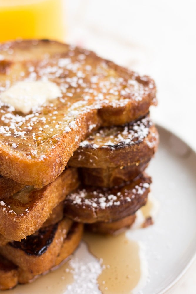 stack of vegan french toast on a plate with butter, powdered sugar and syrup.