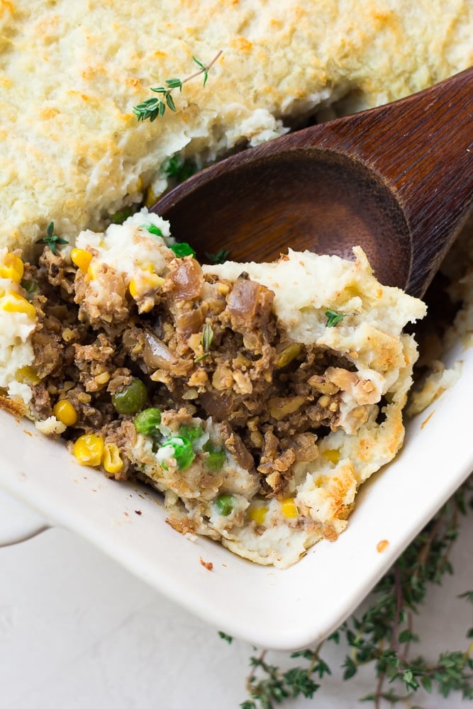 wooden spoon scooping out some vegan shepherd's pie from the casserole dish.