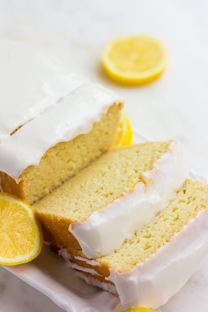 sliced lemon loaf with glaze and lemons in background