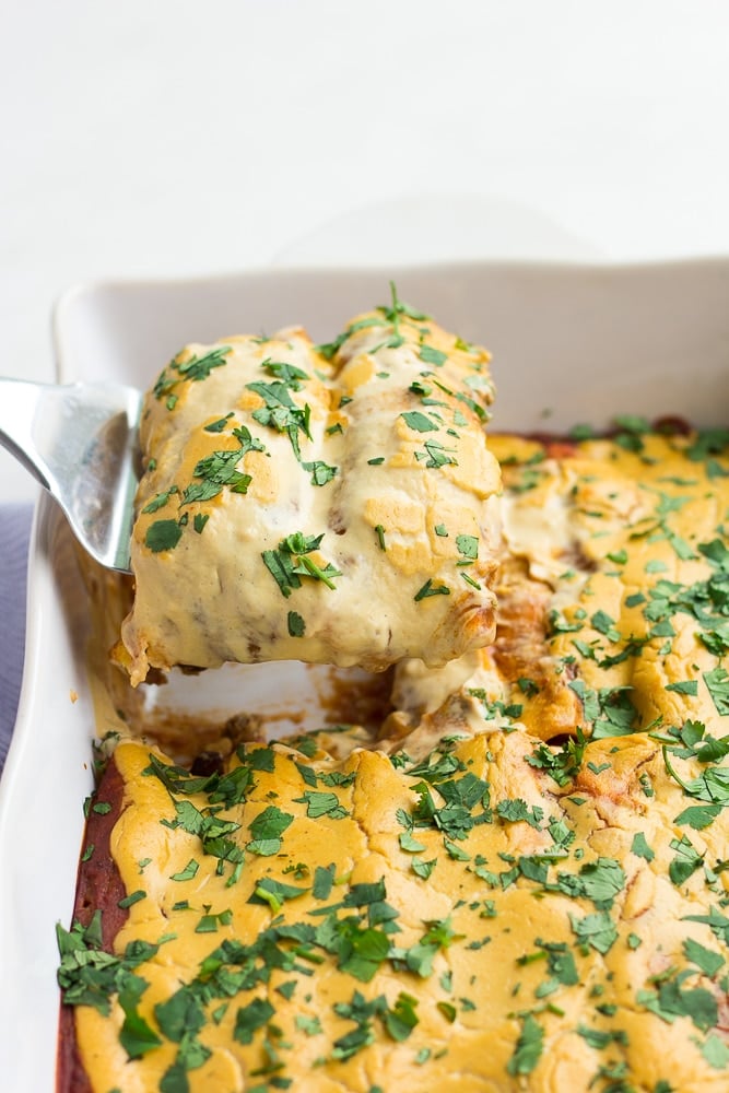 vegan enchiladas being lifted out of casserole dish