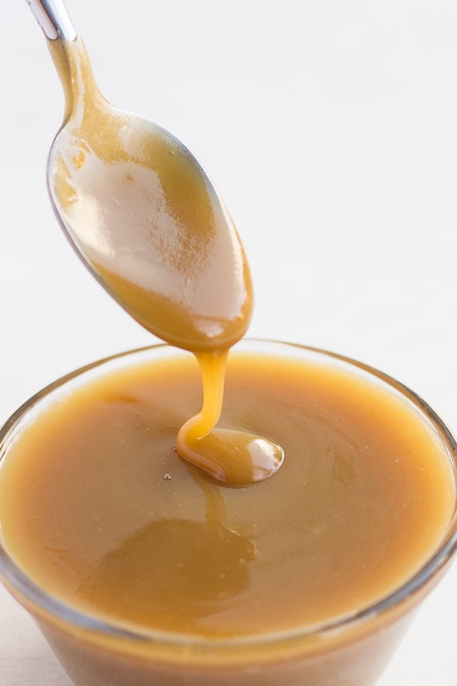 vegan caramel being drizzled with a spoon into a bowl of caramel.