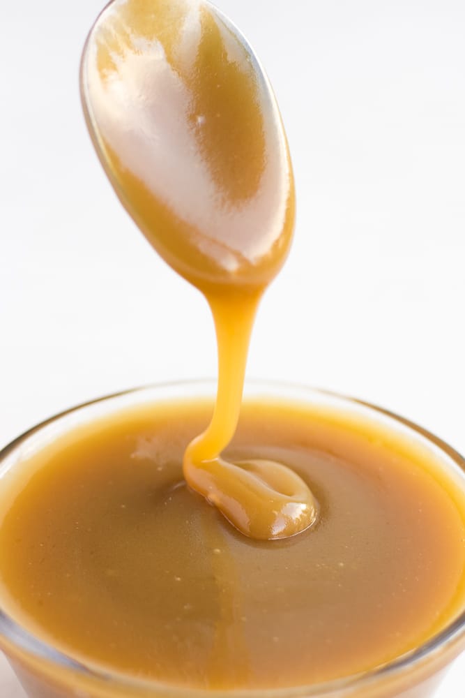 vegan caramel being drizzled with a spoon into a bowl of caramel.