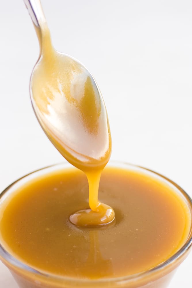 vegan caramel being drizzled with a spoon into a bowl of caramel.