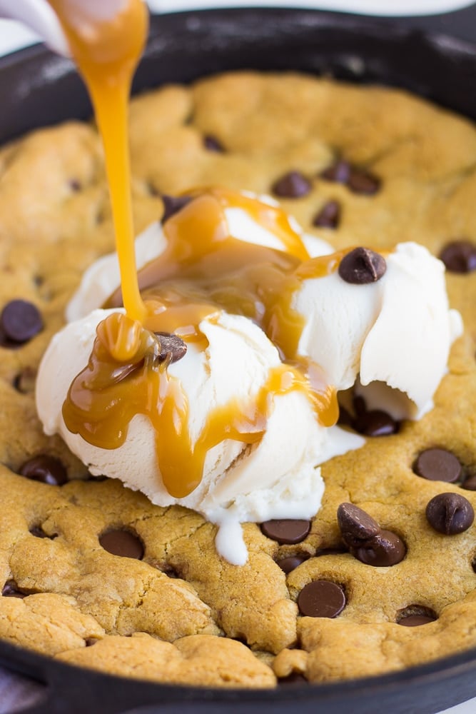 vegan skillet cookie with caramel being poured on top with ice cream.