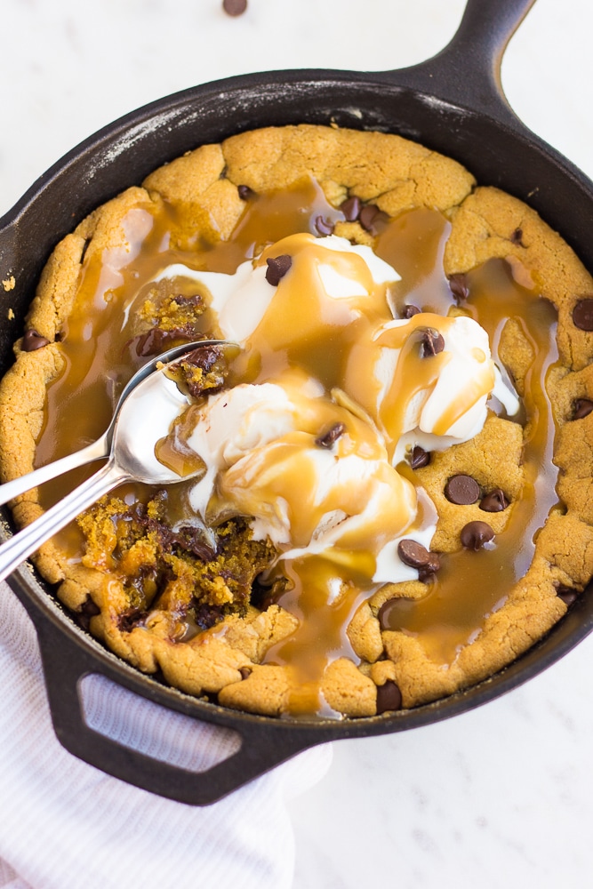 vegan skillet cookie with caramel and ice cream and spoons from above.