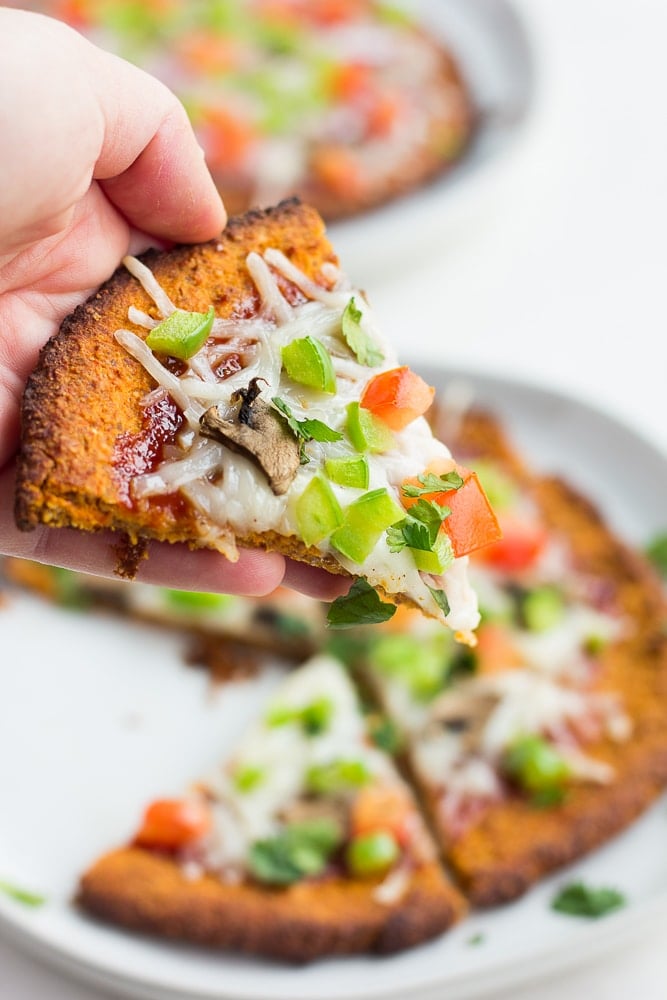 hand holding sweet potato pizza crust with toppings, cooked.