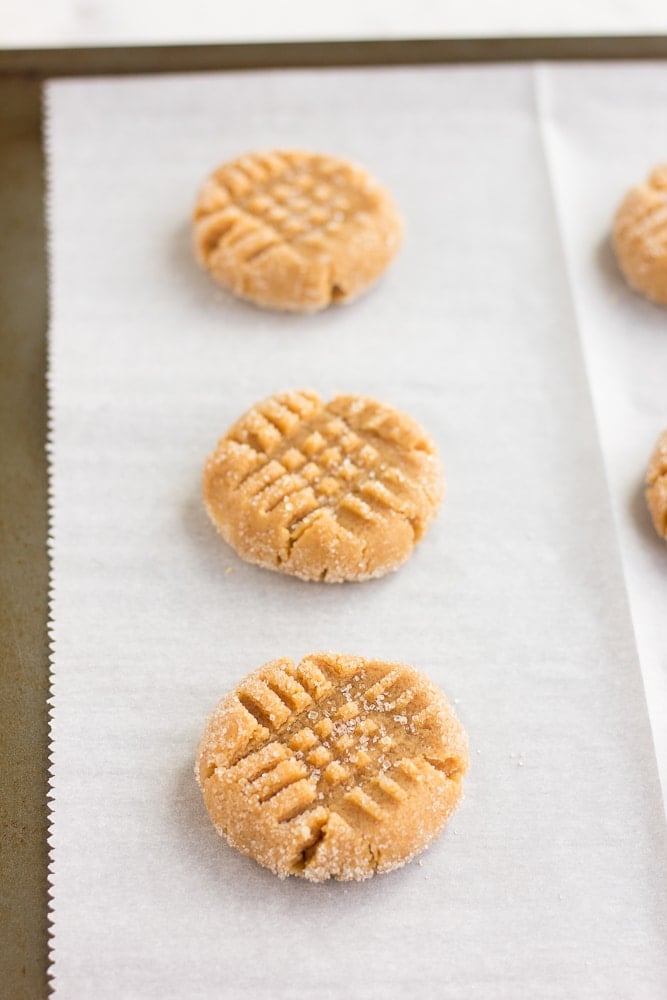 vegan peanut butter cookies on parchment paper, before baking with a criss cross in them.