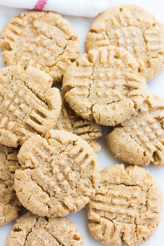 lots of vegan peanut butter cookies, on top of each other, white background.