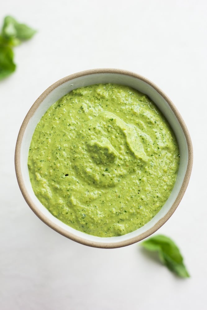 small bowl of vegan pesto, leaves of basil in background