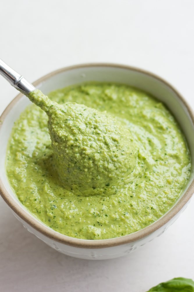 spoonful being taken out of a bowl with pesto in it, white background.