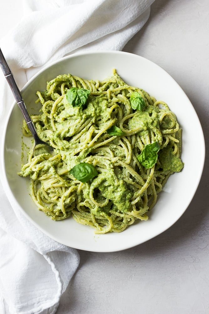 bowl of pasta drenched in pesto sauce, white bowl and background.