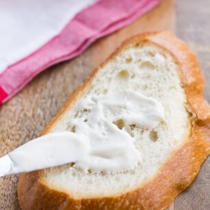 vegan mayo being spread on a piece of bread with a towel in background.