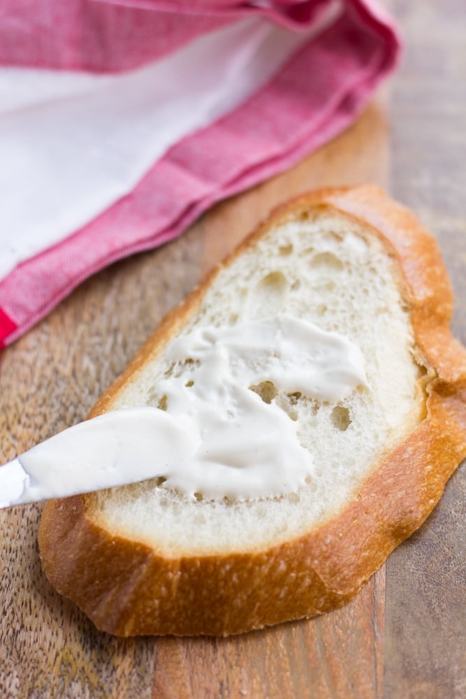 vegan mayo being spread on a piece of bread with a towel in background.