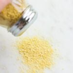 vegan parmesan being sprinkled out of container onto marble background.