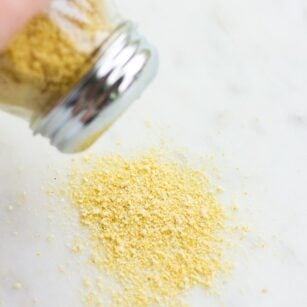 vegan parmesan being sprinkled out of container onto marble background.