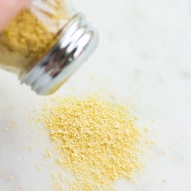 vegan parmesan being sprinkled out of container onto marble background.