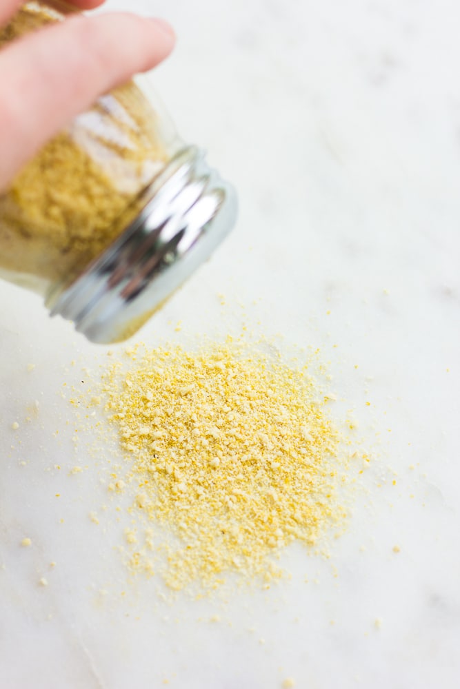 vegan parmesan being sprinkled out of container onto marble background.