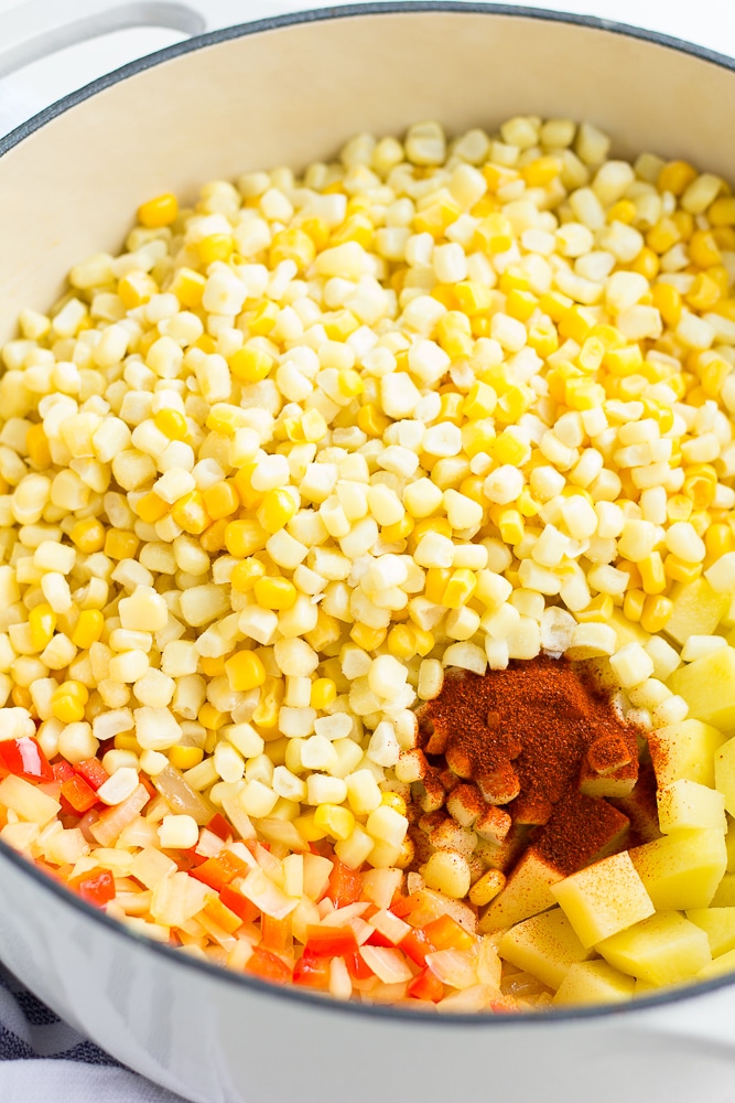 ingredients for vegan corn chowder being added to a large white pot.