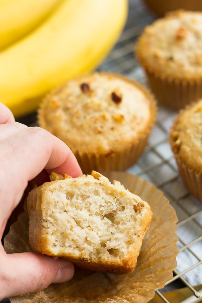 cut in half vegan banana muffin, banana and more muffins in background.