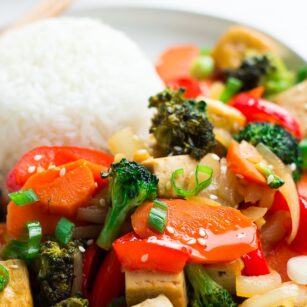 close up photo of tofu stir fry on a plate with rice and chopsticks.