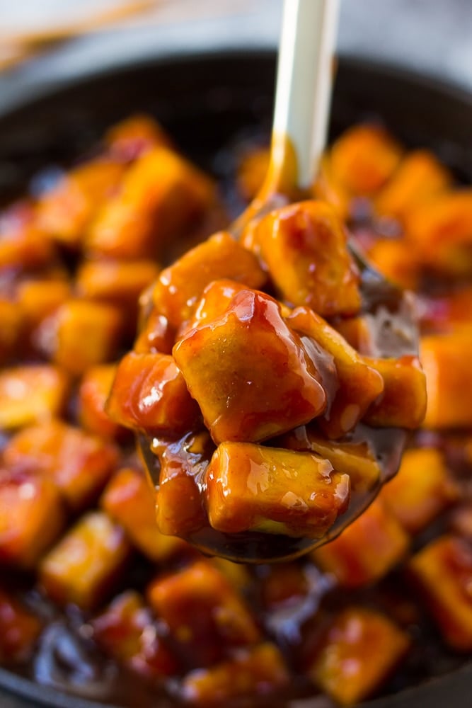 sriracha tofu in a pan being lifted out by a silver spoon