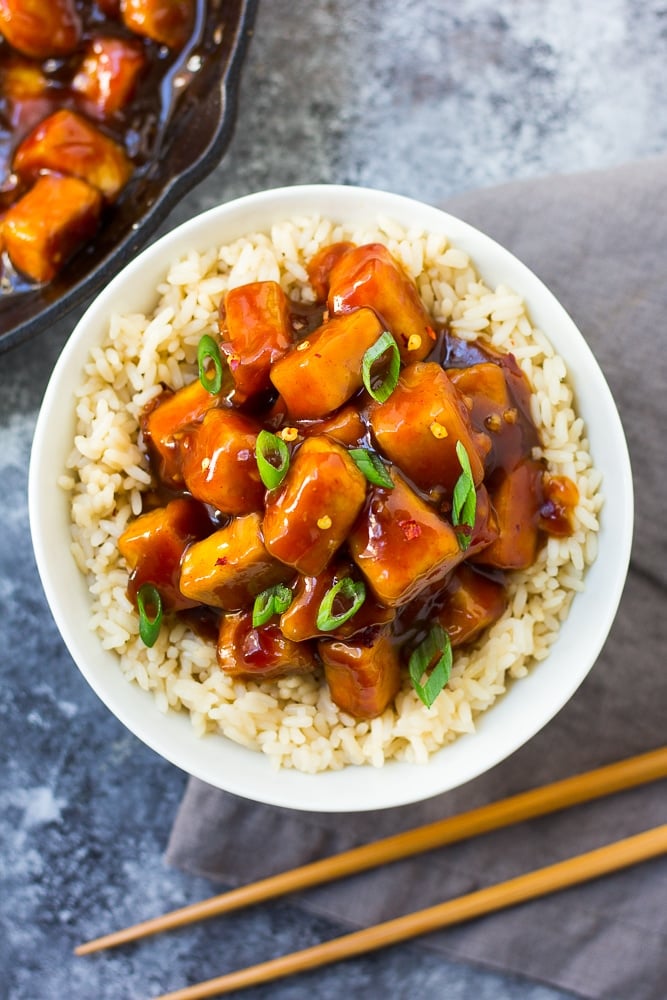 looking down on a bowl of sriracha tofu with chopsticks and green onions.