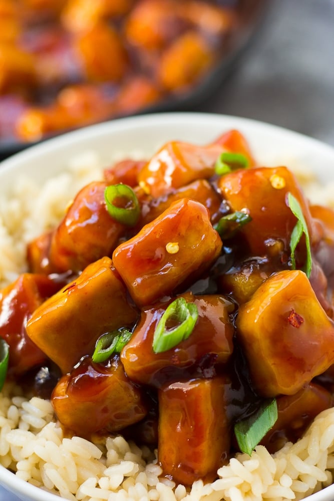 very close up photo of sriracha tofu in bowl with green onions