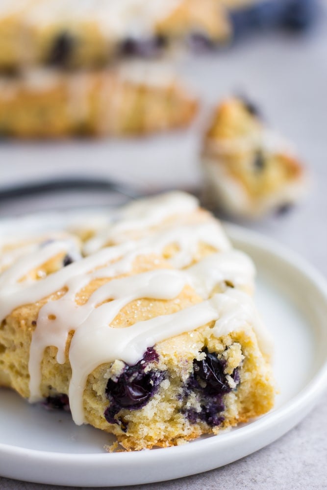 one vegan blueberry scone on a white plate with more scones in background.