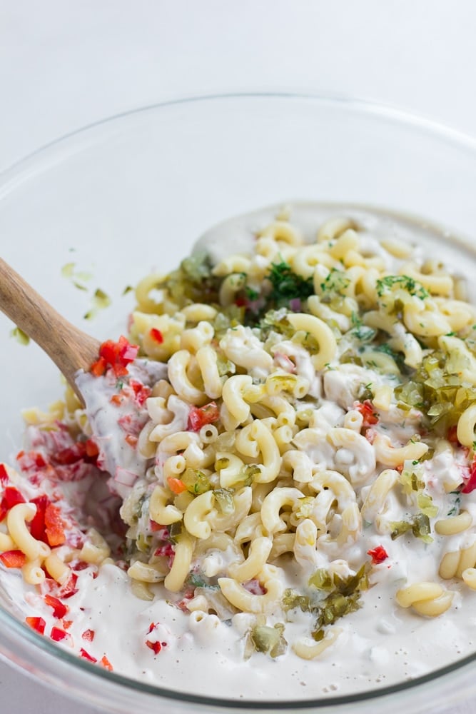 stirring macaroni salad ingredients together in a large clear bowl.