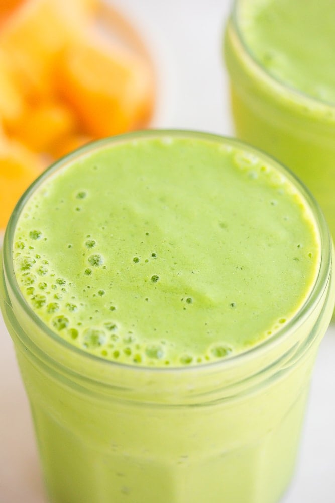 close up of vegan green smoothie with mango in background.