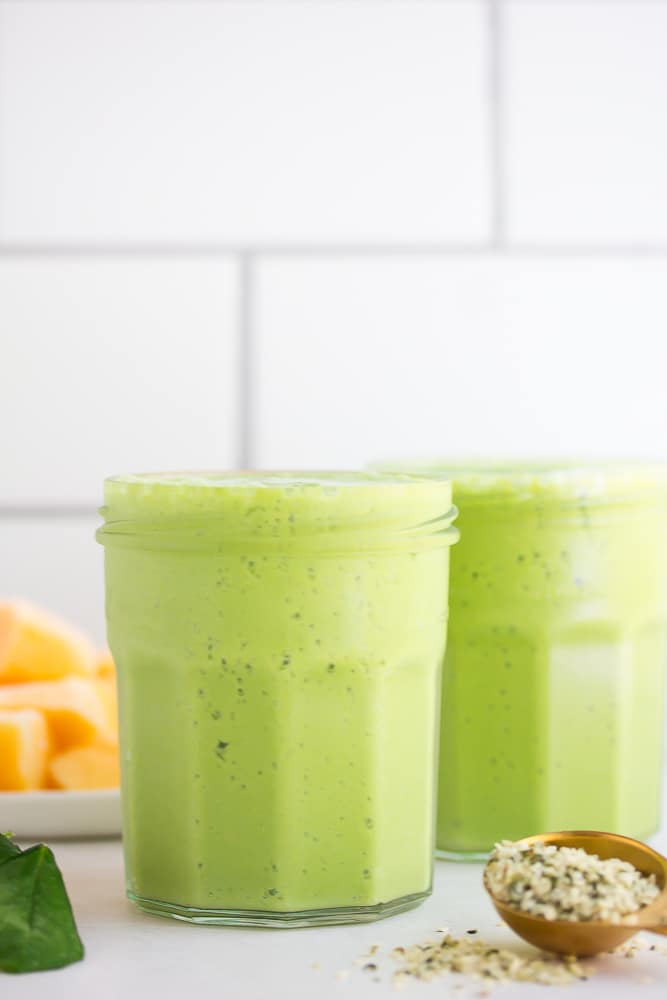 tile background and vegan green smoothies in 2 cups, mango in back.