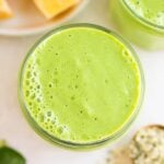 looking down close up on vegan green smoothie with mango and leaves in background.