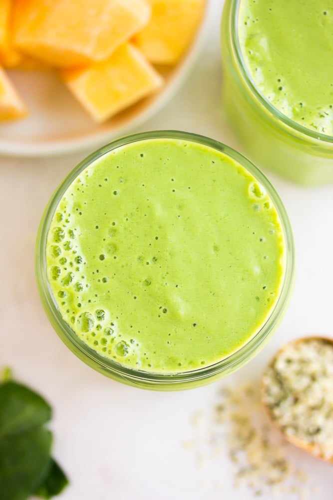 looking down close up on vegan green smoothie with mango and leaves in background.