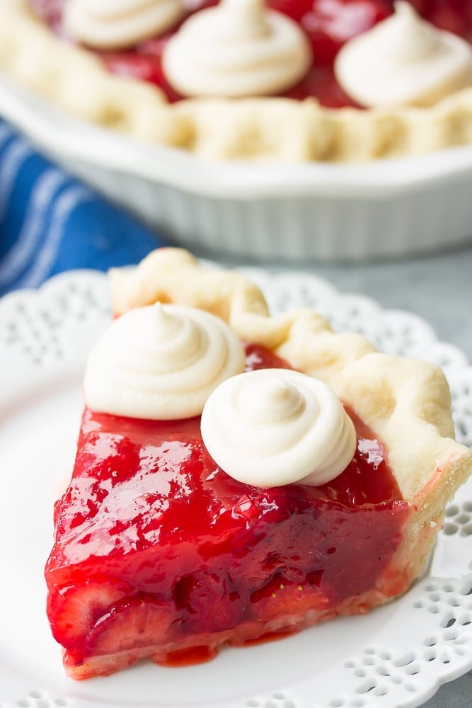 slice of strawberry pie on a white plate, blue towel in background.