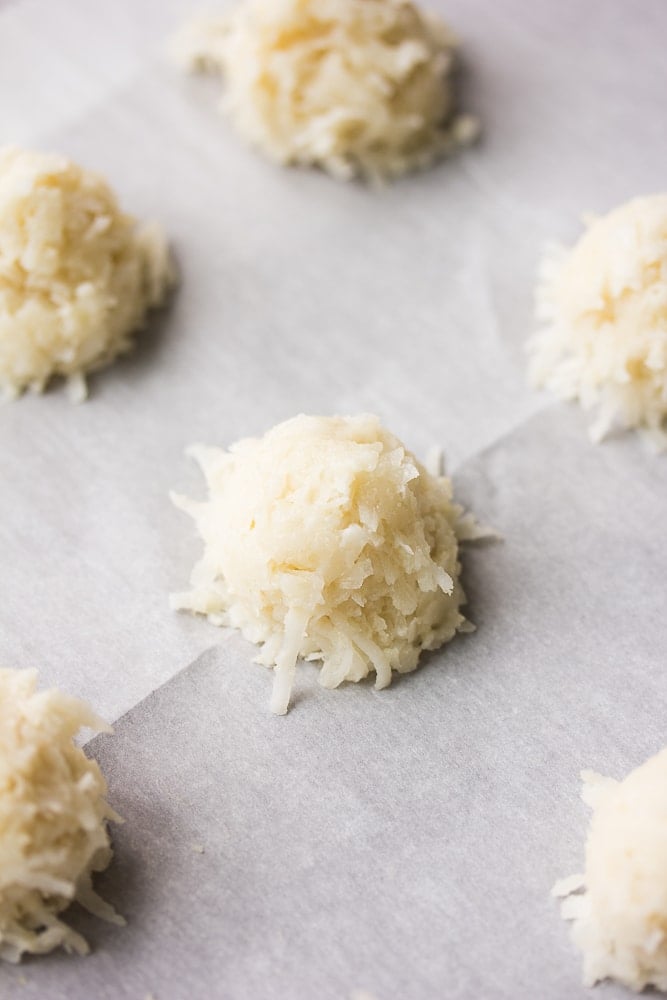 uncooked balls of coconut cookie dough on parchment lined pan.