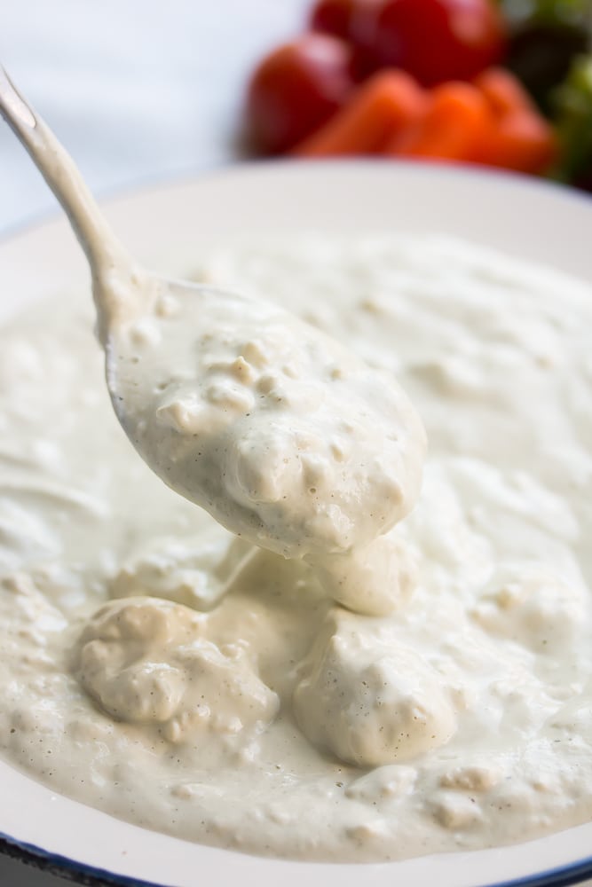 spoon being lifted from a bowl of chunky white dressing.