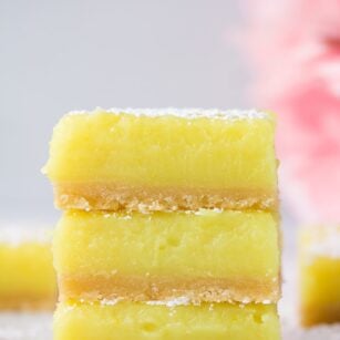 3 stacked vegan lemon bars with pink flowers in background