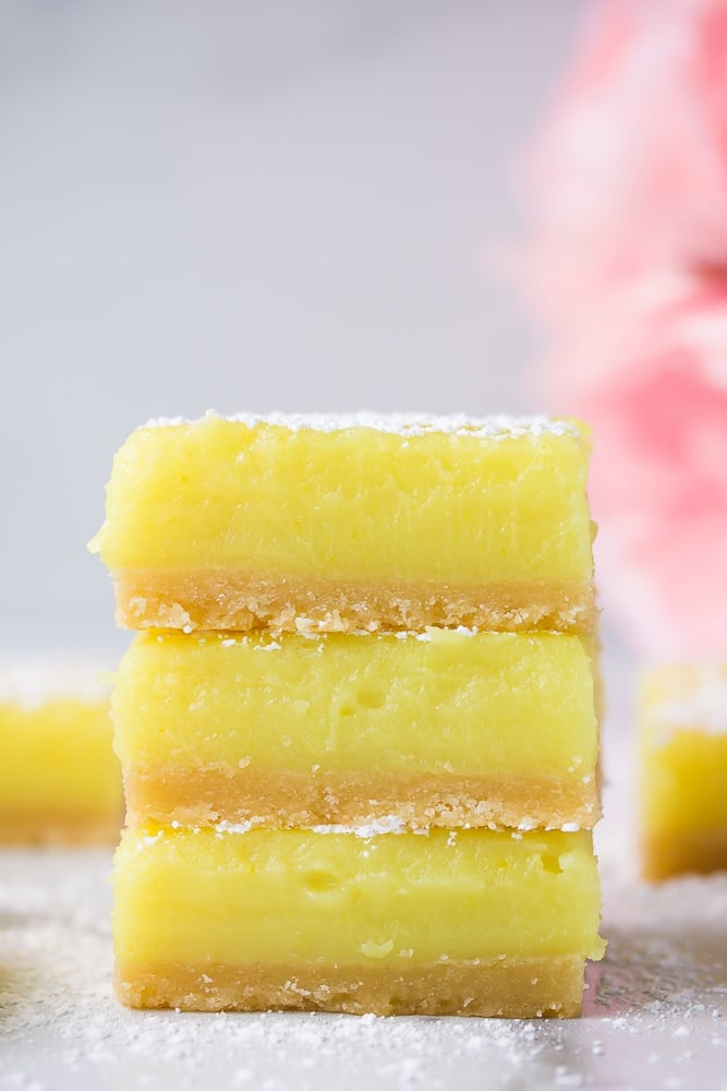 3 stacked vegan lemon bars with pink flowers in background