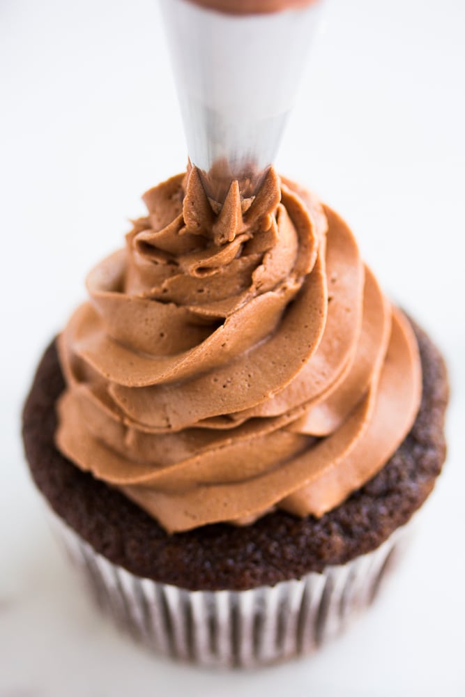 vegan chocolate frosting being piped onto a cupcake