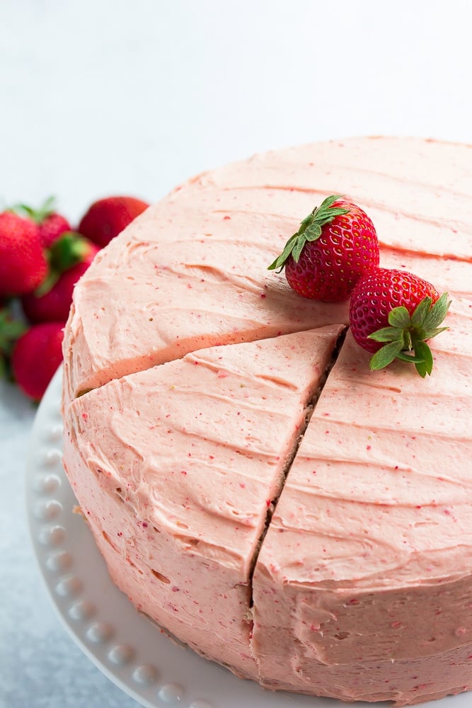 whole cake, with 1 sliced, strawberries on top and in back