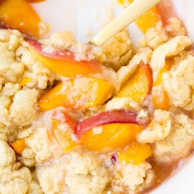 close up of vegan peach casserole in dish with a gold spoon