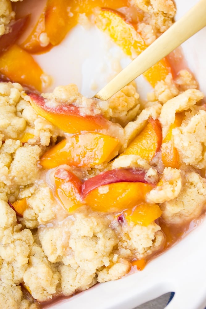 close up of vegan peach casserole in dish with a gold spoon