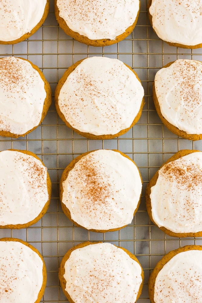 lots of frosted vegan pumpkin cookies on a baking sheet