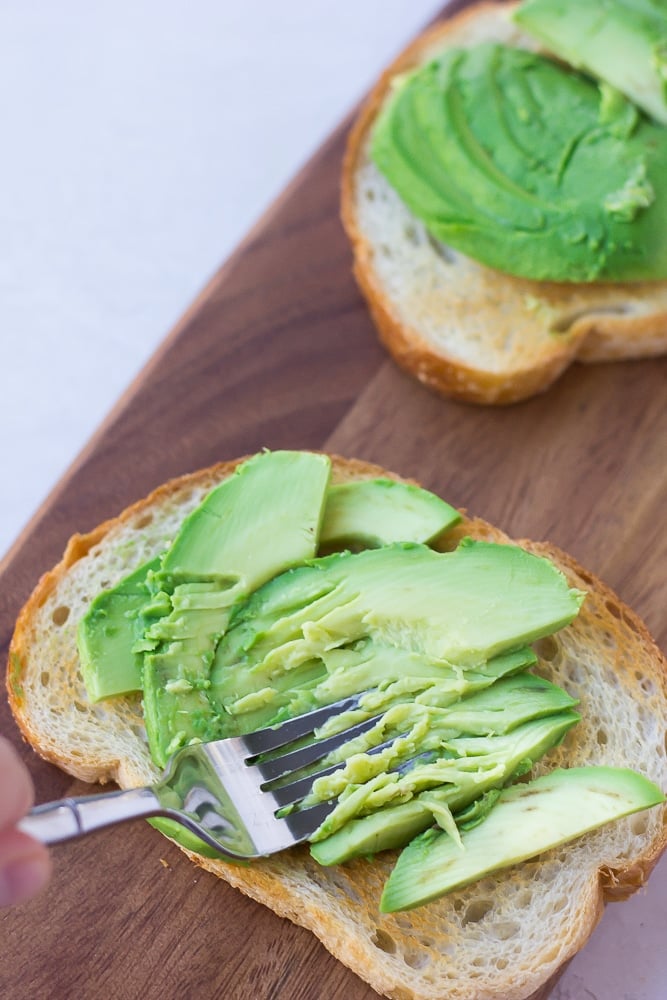 showing mashing avocado on sourdough bread with a fork