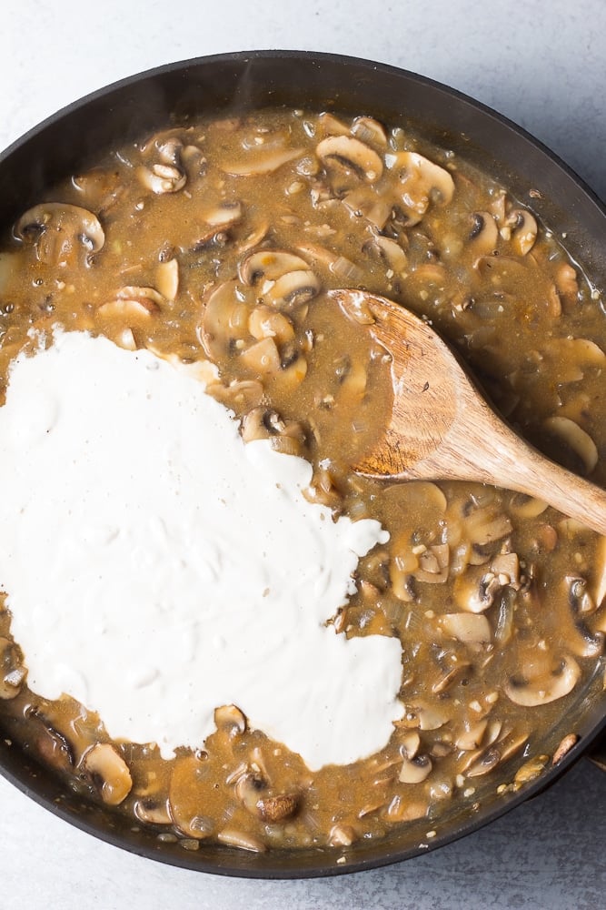 cashew cream being added to a pan with mushrooms