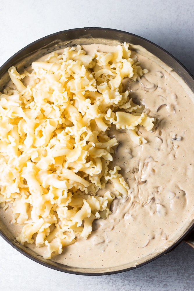 noodles being added to a pan with mushroom gravy