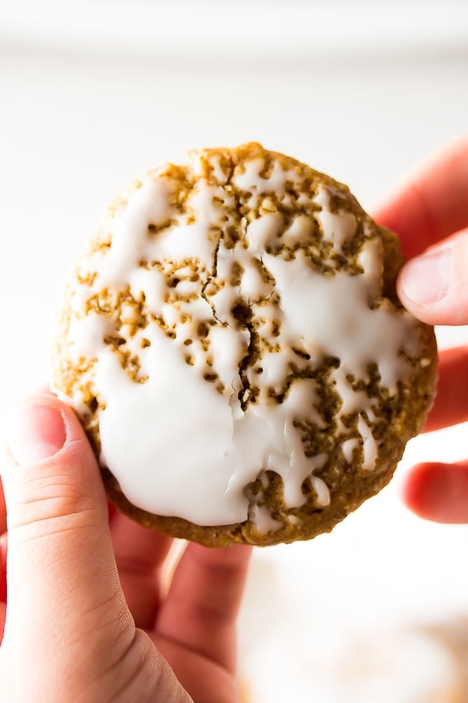 close up of a iced oatmeal cookie with hands pulling it apart.