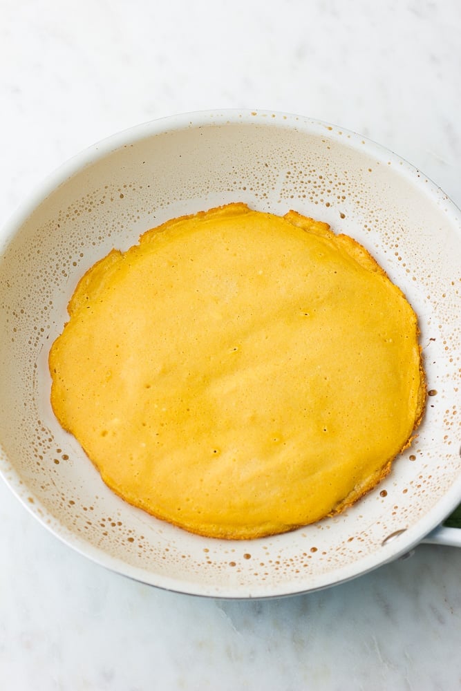 plain vegan omelette cooking in a white pan