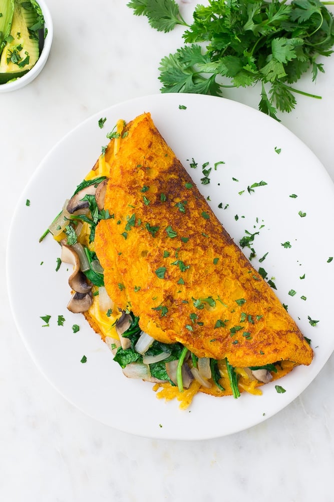 looking down on a vegan omelette on a white plate with cilantro all over it