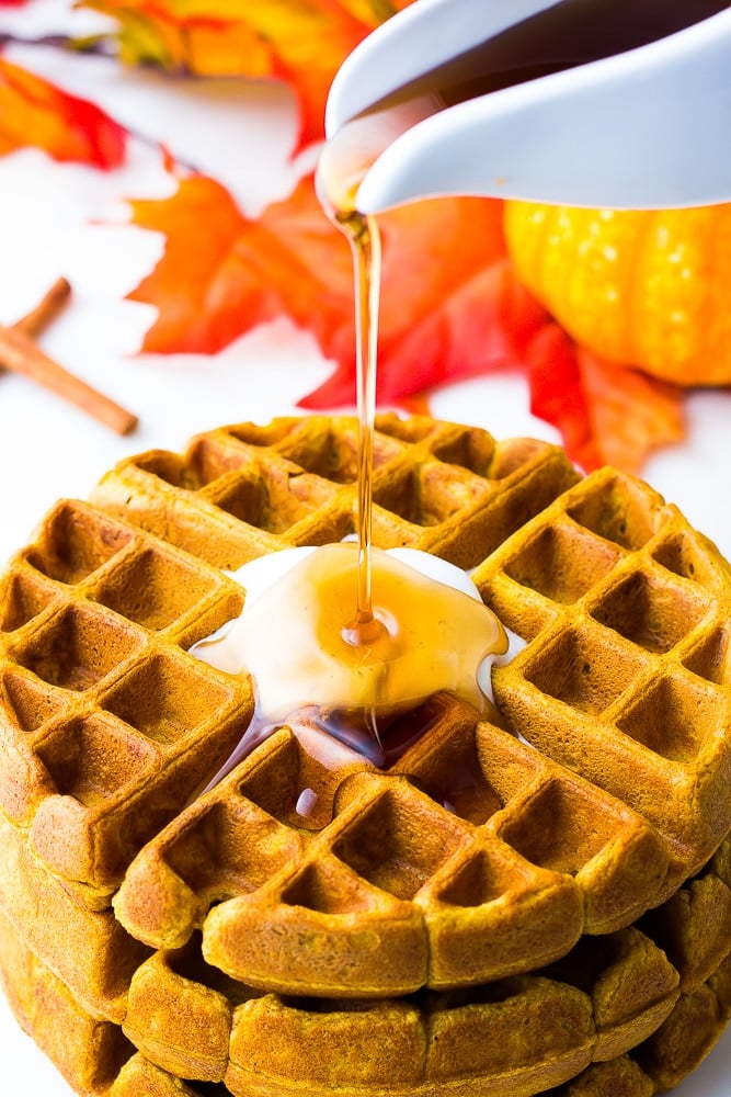 syrup pouring onto vegan pumpkin waffles with leaves and pumpkins in background